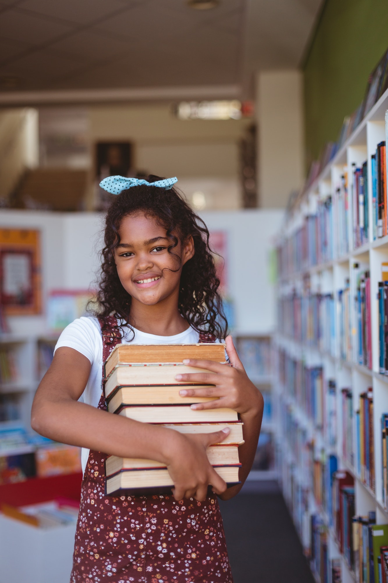 portrait-of-smiling-african-american-schoolgirl-carrying-stack-of-books-in-school-library.jpg